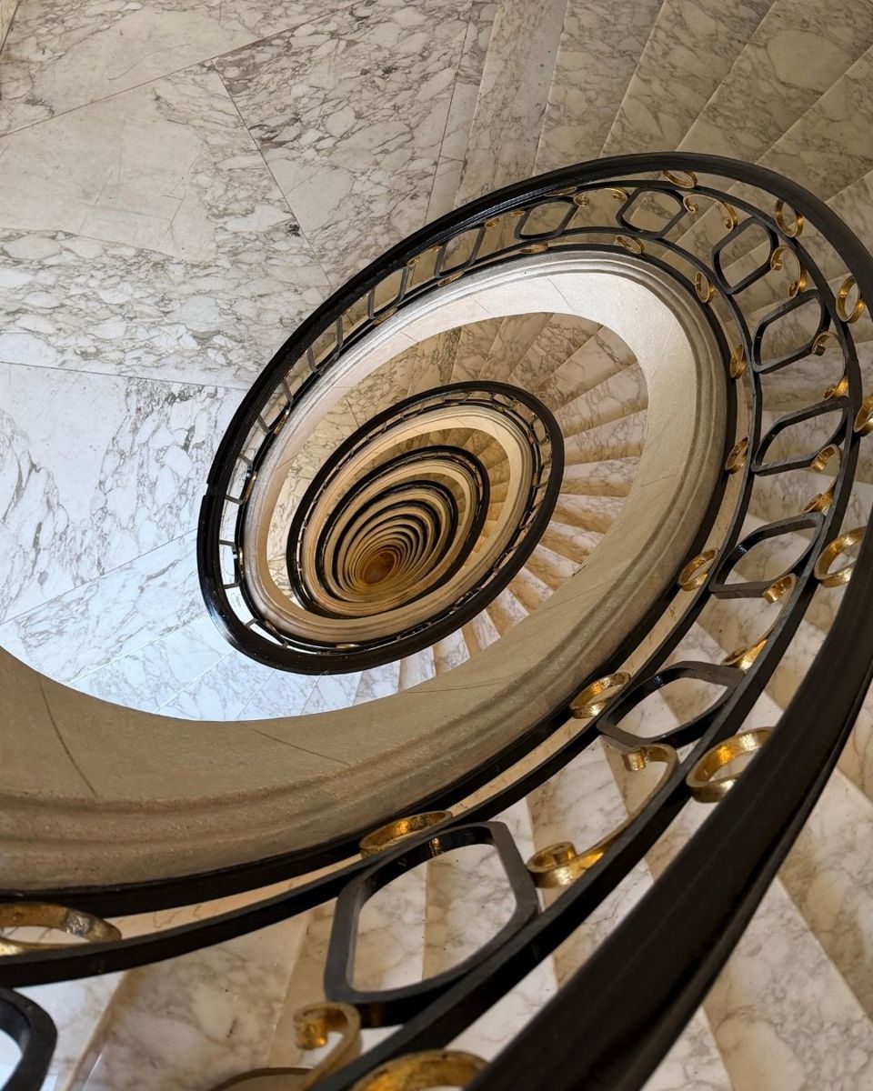 Escadaria em espiral de mármore com corrimão preto e dourado